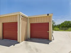 Exterior corner of tan metal storage building with red roll-up doors and a security camera