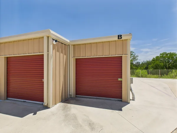 Exterior corner of tan metal storage building with red roll-up doors and a security camera