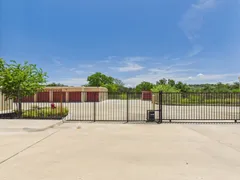 A gated entrance to a storage facility with red roll-up doors and a concrete driveway