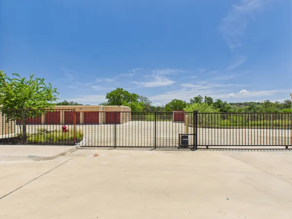 A gated entrance to a storage facility with red roll-up doors and a concrete driveway