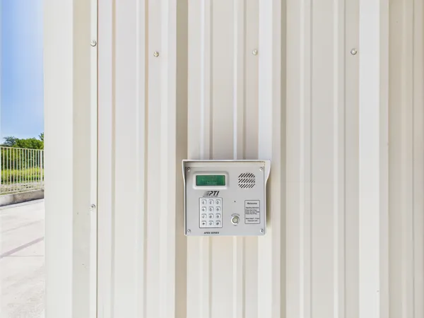 A wall-mounted electronic keypad for secure gate access on a beige corrugated metal storage building exterior