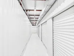 Brightly lit indoor storage hallway with white corrugated metal walls and several roll-up unit doors