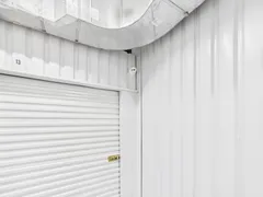 A white roll-up storage door with a latch and a security camera mounted above it