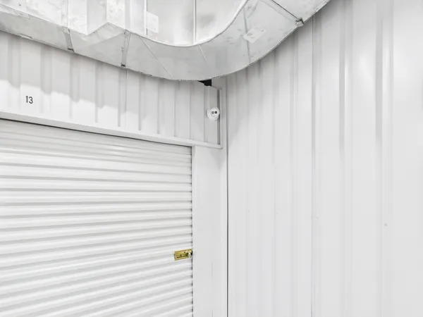 A white roll-up storage door with a latch and a security camera mounted above it