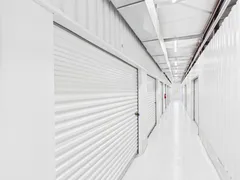 Bright indoor hallway with white roll-up storage unit doors and fluorescent lighting overhead