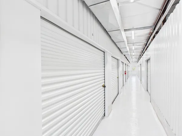 Bright indoor hallway with white roll-up storage unit doors and fluorescent lighting overhead