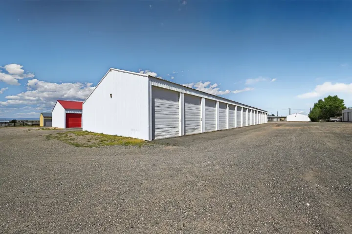 Row of white drive-up storage units in Laramie on Skyline Road, with roll-up doors along a paved driveway under a blue sky