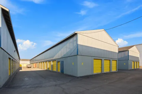Multiple rows of outdoor storage buildings with yellow roll-up doors and asphalt driving lanes under blue sky