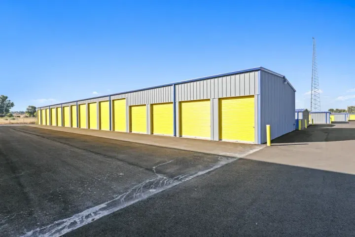 Outdoor storage building featuring a row of yellow roll-up doors and a wide paved driving aisle