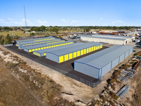 Aerial view of several long rows of self-storage units with yellow doors and metal roofs