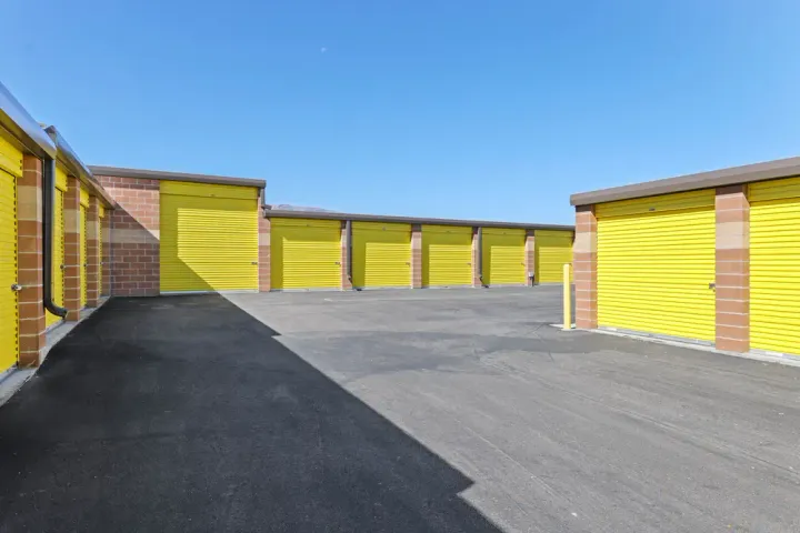 Outdoor drive-up self-storage units with yellow roll-up doors and brick pillars under a clear blue sky