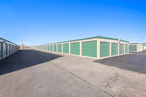 Rows of outdoor drive-up storage units in Laramie with green roll-up doors and asphalt driveways under a blue sky