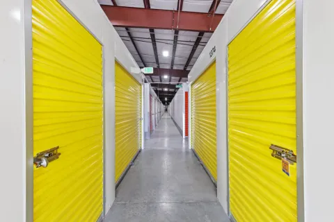 Indoor storage facility hallway featuring bright yellow roll-up unit doors and concrete flooring under LED lighting