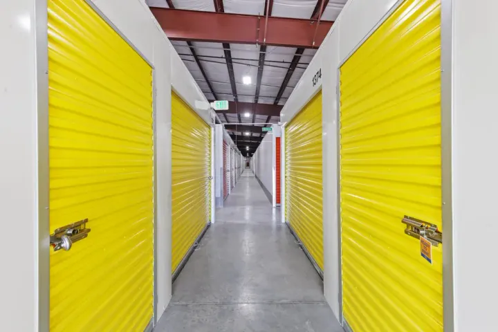 Indoor storage facility hallway featuring bright yellow roll-up unit doors and concrete flooring under LED lighting