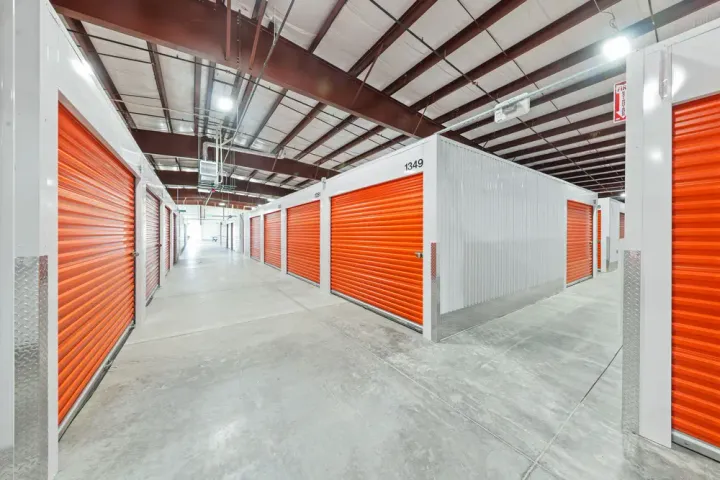 Indoor hallway of a climate controlled storage facility with rows of orange roll-up doors and white walls