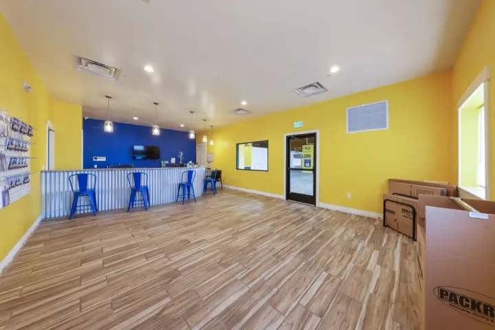 Storage facility office with yellow walls, corrugated metal counter, blue barstools, and moving boxes for sale