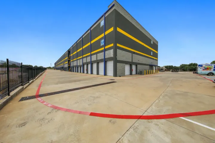 Multi-story self-storage building with yellow stripes, white roll-up doors, and a wide concrete driving area