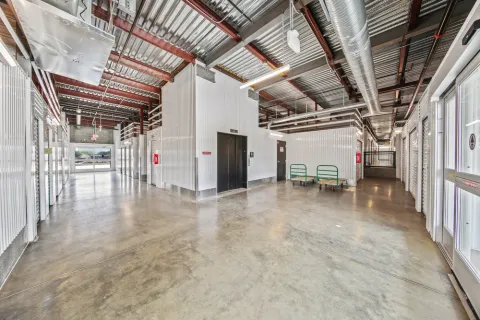 Indoor storage facility hallway with concrete floors, an elevator, white corrugated units, and two green moving carts