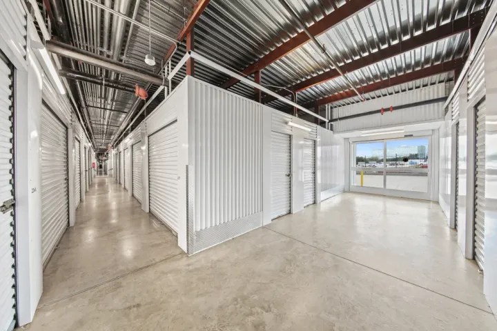 Indoor hallway with white roll-up storage unit doors, concrete floors, and a sliding glass entrance door