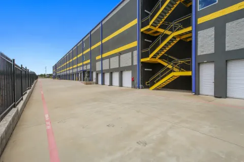 Multistory self-storage facility with grey and yellow exterior walls, white roll-up doors, and an outdoor staircase