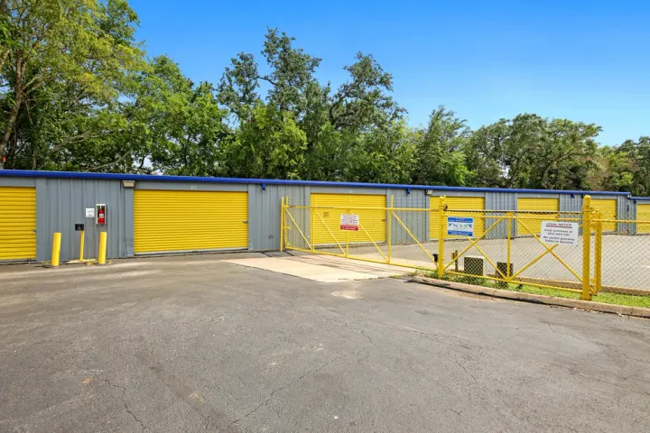 Outdoor storage unit building with yellow roll-up doors and a matching yellow chain-link security gate