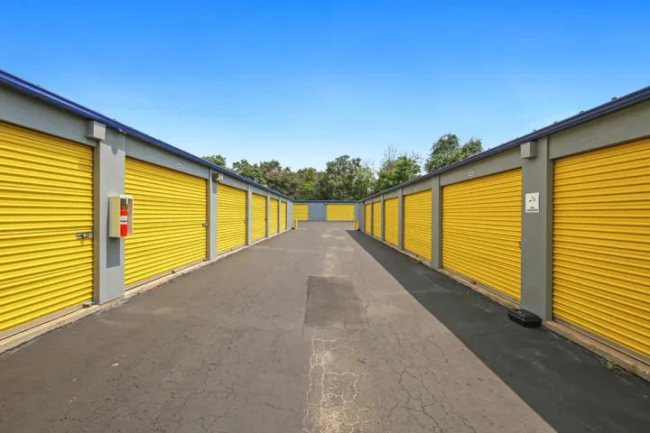 Rows of outdoor drive-up storage units with yellow roll-up doors along a paved asphalt driveway