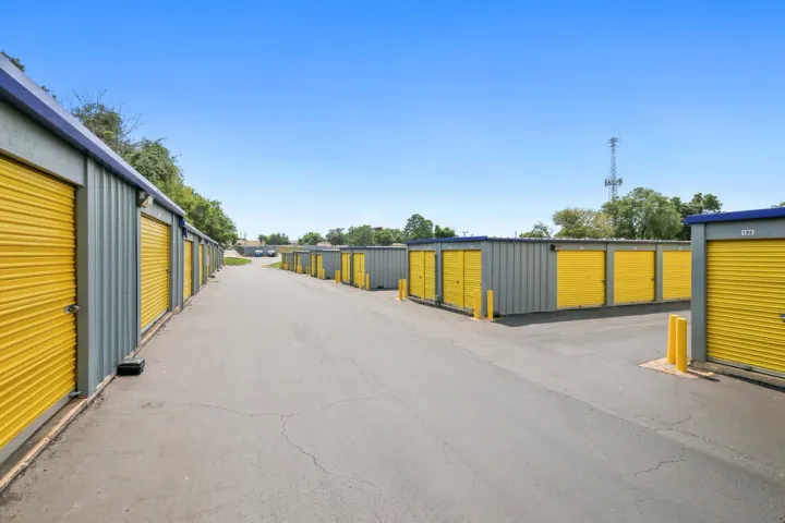 Rows of outdoor drive-up storage units with yellow roll-up doors and gray metal siding along asphalt paths